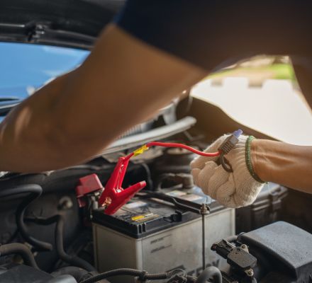 Mechanic connecting jumper cables to a car battery under the hood.