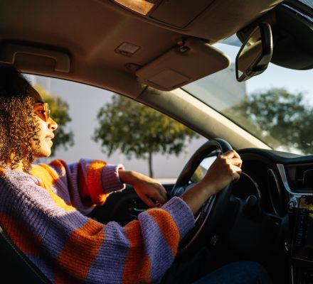 Woman driving a car with sunlight streaming through the windshield.